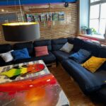 Gemütliche Lounge mit einem schwarzen Sofa und bunten Kissen im modernen Design natürliche Beleuchtung durch Fenster Holztisch mit künstlerischem Motiv im Vordergrund Gemütliche Lounge mit einem schwarzen Sofa und bunten Kissen im modernen Design natürliche Beleuchtung durch Fenster Holztisch mit künstlerischem Motiv im Vordergrund