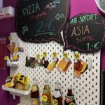 Lebensmittelpräsentation mit asiatischen Instant-Suppen Flaschen mit asiatischen Saucen und Pizzen auf Regal vor lila Hintergrund Werbetafeln mit Angeboten sichtbar