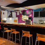 Bunte und moderne Café-Bar mit farbenfroher Einrichtung in der Schweiz. Helle Hocker an der Theke und stilvolle Dekoration schaffen eine einladende Atmosphäre.